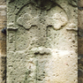 Sandsteinepitahp mit verwitterter Inschrift und Kreuz im Bogenfeld. 