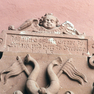 Name und Jahreszahl als Bauinschrift auf einer Wappentafel aus rotem Sandstein.