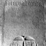 Fragment einer Grabplatte mit den Grabinschriften für eine unbekannte Person (Nr. 276) und die Ehefrau und Kinder des Stephan Harmair (Nr. 520), an der Westwand im elften Abschnitt von Norden, obere Platte. Mehrfachverwendung. Rotmarmor.