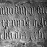 Fragment einer Grabplatte an der Westwand des Querhauses, zweite Platte von Süden in der mittleren Reihe. Rotmarmor. Behauen.