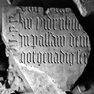 Fragment einer Grabplatte mit Resten einer Inschrift in Gotischer Majuskel. Rotmarmor.