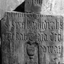 Fragment einer Priestergrabplatte aus rotem Marmor, an der Wand aufgerichtet.