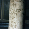 Stifterinschrift und Bibelzitat auf dem Fuß eines Taufbeckens aus grauem Sandstein 