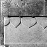 Fragment einer Grabplatte, an der Westwand, innen unter der Empore, achte Platte von Norden, untere Reihe. Rotmarmor.