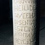 Stifterinschrift und Bibelzitat auf dem Fuß eines Taufbeckens aus grauem Sandstein 