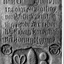 Fragment der Grabplatte für Wolfgang Haytzinger, an der Wand neben der Tür zur Sakristei (Westwand des Querhauses), dritte von Süden, in der Mitte. Rotmarmor.